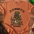 Orange t-shirt with graphic of a monster sitting on a mushroom, drinking coffee. Text reads "It is what it is and it's pretty terrible."
