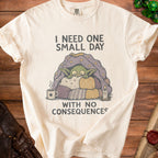 Cream t-shirt with graphic of a creature under a blanket saying "I NEED ONE SMALL DAY WITH NO CONSEQUENCES".