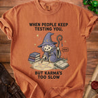 Orange t-shirt with a wizard and pentagram design reading "When people keep testing you, but karma's too slow."