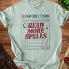 Light blue t-shirt with "Grimoire Card Read More Spells" graphic and library card details.