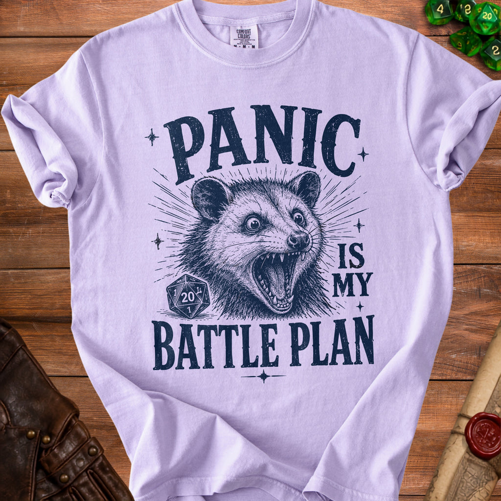 Light purple t-shirt with a distressed print of a possum, a D20 die, and the text "PANIC IS MY BATTLE PLAN".