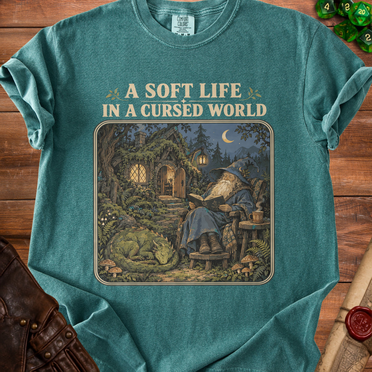 Green t-shirt with "A Soft Life In A Cursed World" text and wizard, dragon, and cottage illustration.