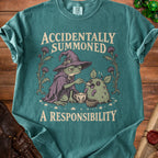 Green t-shirt with a frog wizard feeding a fluffy creature, "Accidentally Summoned A Responsibility" text.