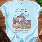 Light blue t-shirt with illustration of a witch and text: "It's Spicy You Won't Like It When People Ask What I'm Thinking".