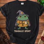 Black t-shirt with a tired wizard frog holding a mug and wand, text "TOADALLY SPENT".