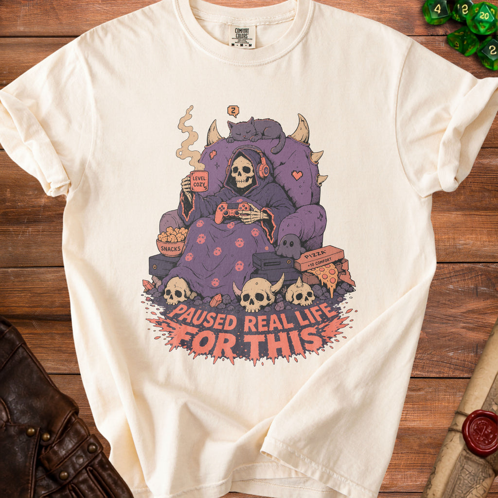 Cream t-shirt with graphic of skeleton gamer in throne with text "Paused Real Life For This".