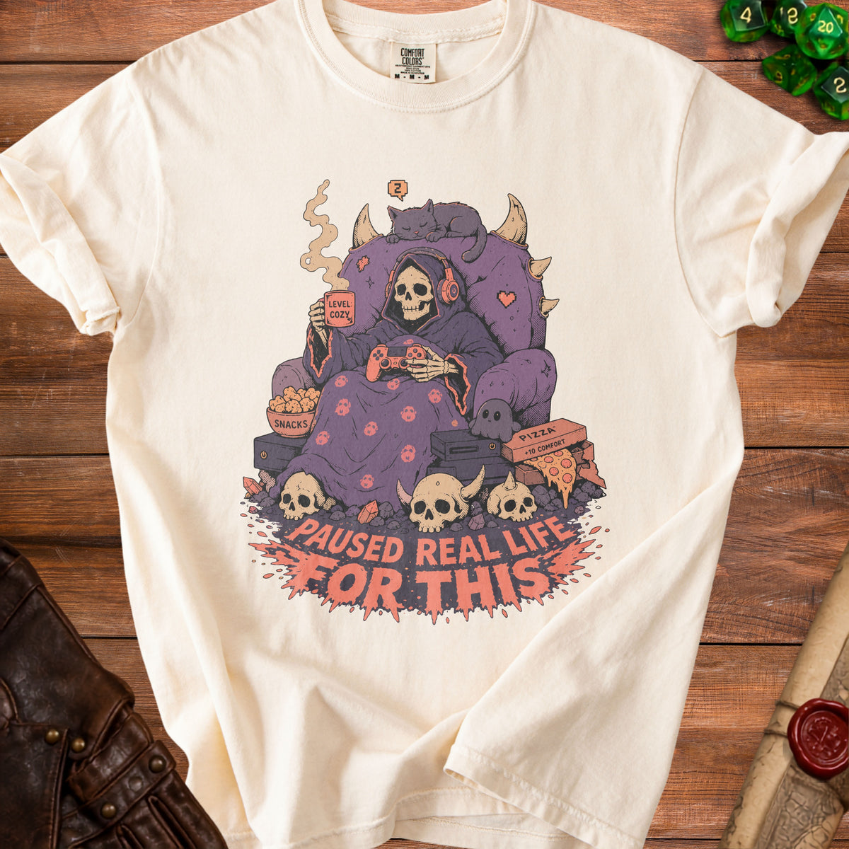 Cream t-shirt with graphic of skeleton gamer in throne with text "Paused Real Life For This".