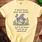 Yellow t-shirt with a mushroom character and text "I don't know what lies ahead... but I do know it will be an adventure".
