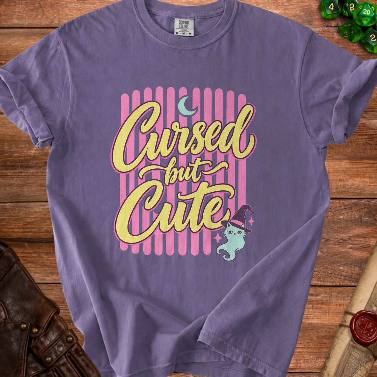 Purple t-shirt with text "Cursed but Cute" and a mint cat in a witch hat.