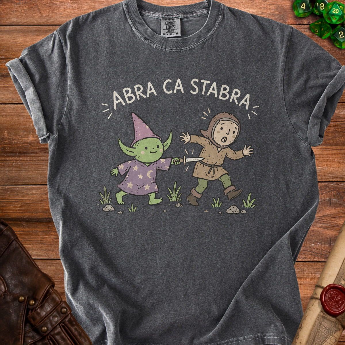 T-shirt with "ABRA CA STABRA" text above a cartoon goblin and a fleeing person.