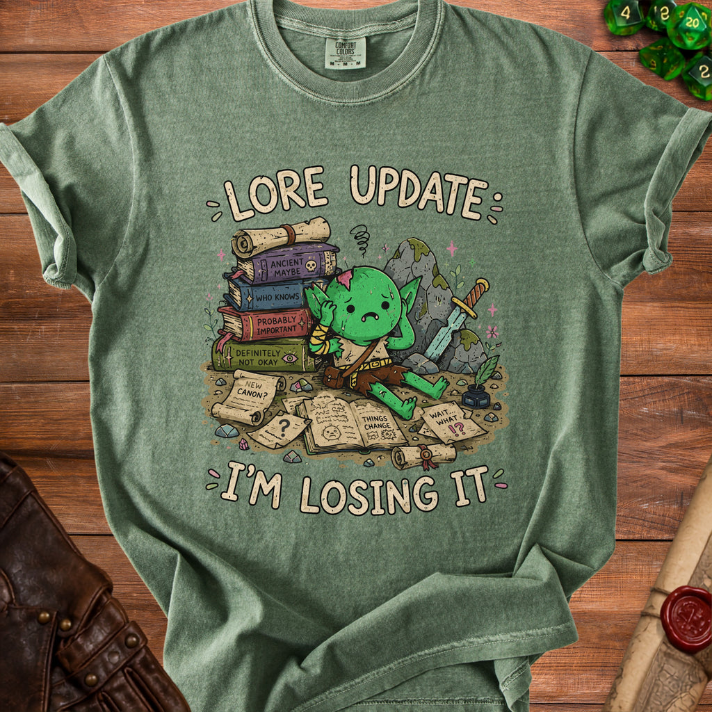 Green t-shirt with cartoon goblin, books, sword, and text "Lore Update: I'm Losing It".