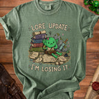 Green t-shirt with cartoon goblin, books, sword, and text "Lore Update: I'm Losing It".
