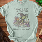 Light green t-shirt with "I HAVE A PHD IN CRAFTING (PROJECTS HALF DONE)" and a goblin crafting illustration.