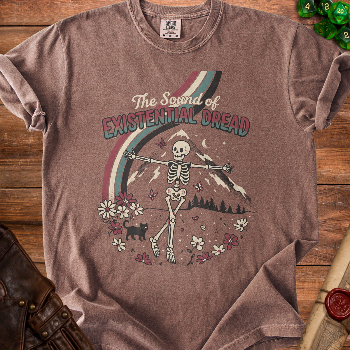 Brown t-shirt with graphic of skeleton dancing, flowers, cat, and text "The Sound of Existential Dread".