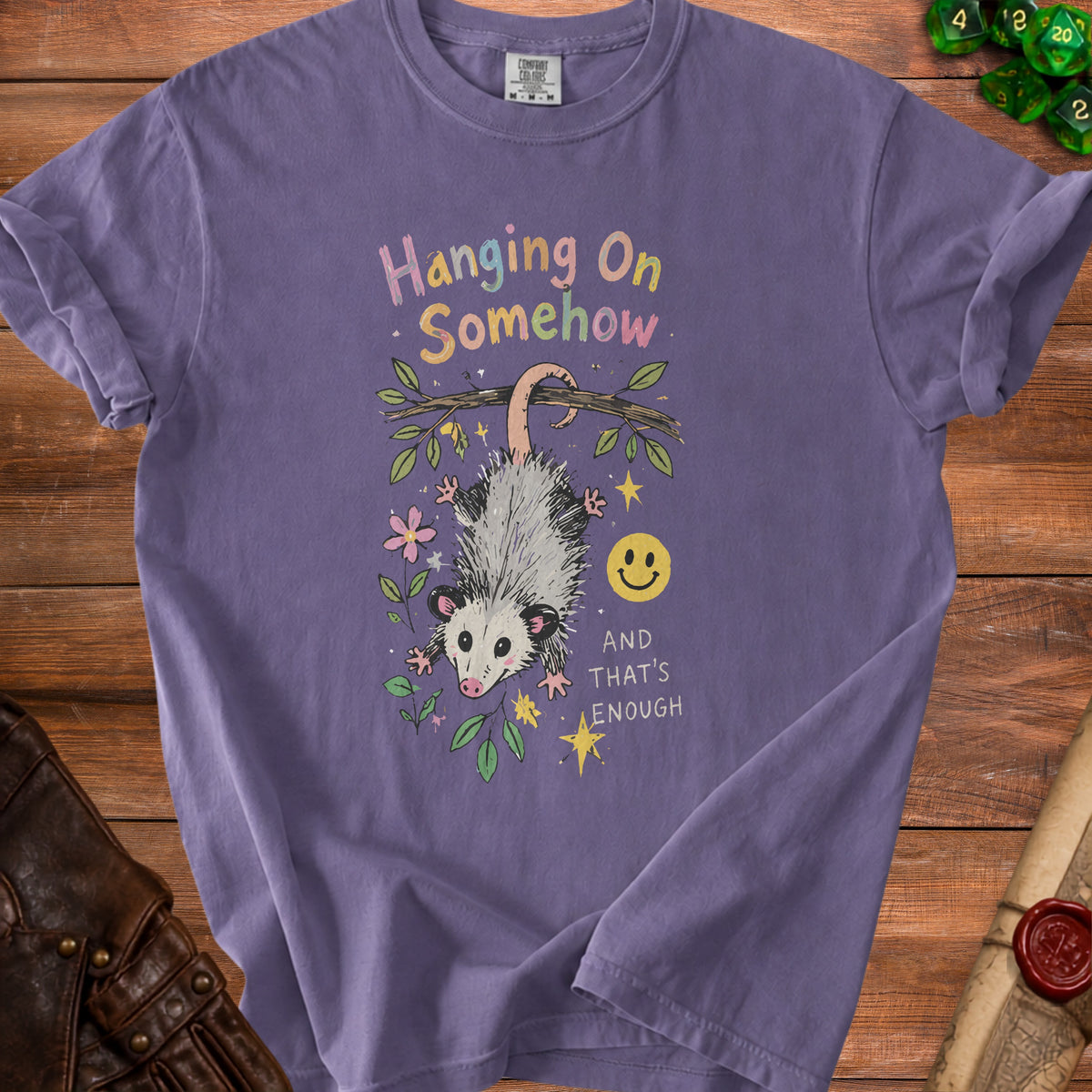 Purple t-shirt with opossum hanging from branch text "Hanging On Somehow" and "And That's Enough".