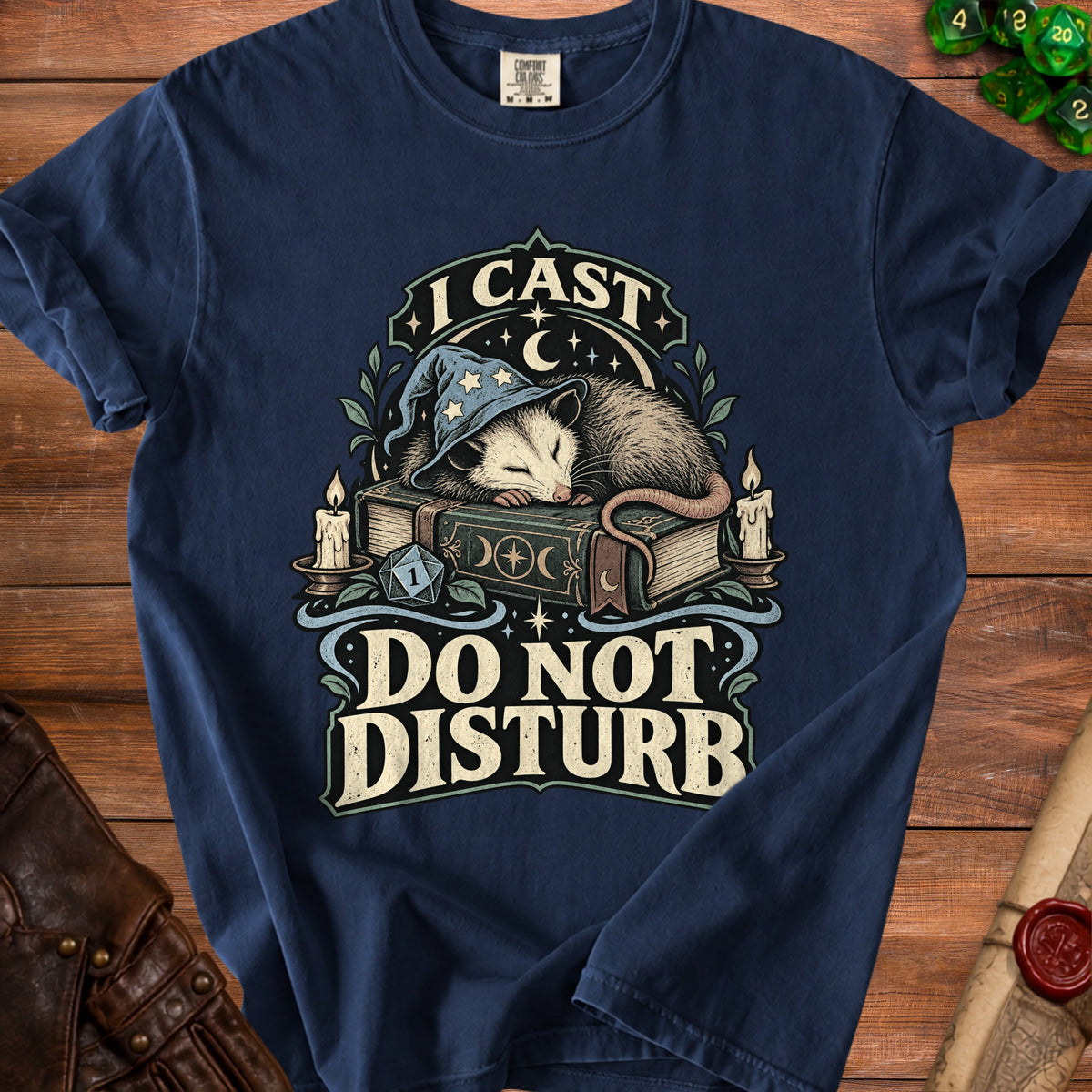 Navy blue t-shirt featuring a graphic of an opossum in a wizard hat sleeping on a book with the text I CAST DO NOT DISTURB.