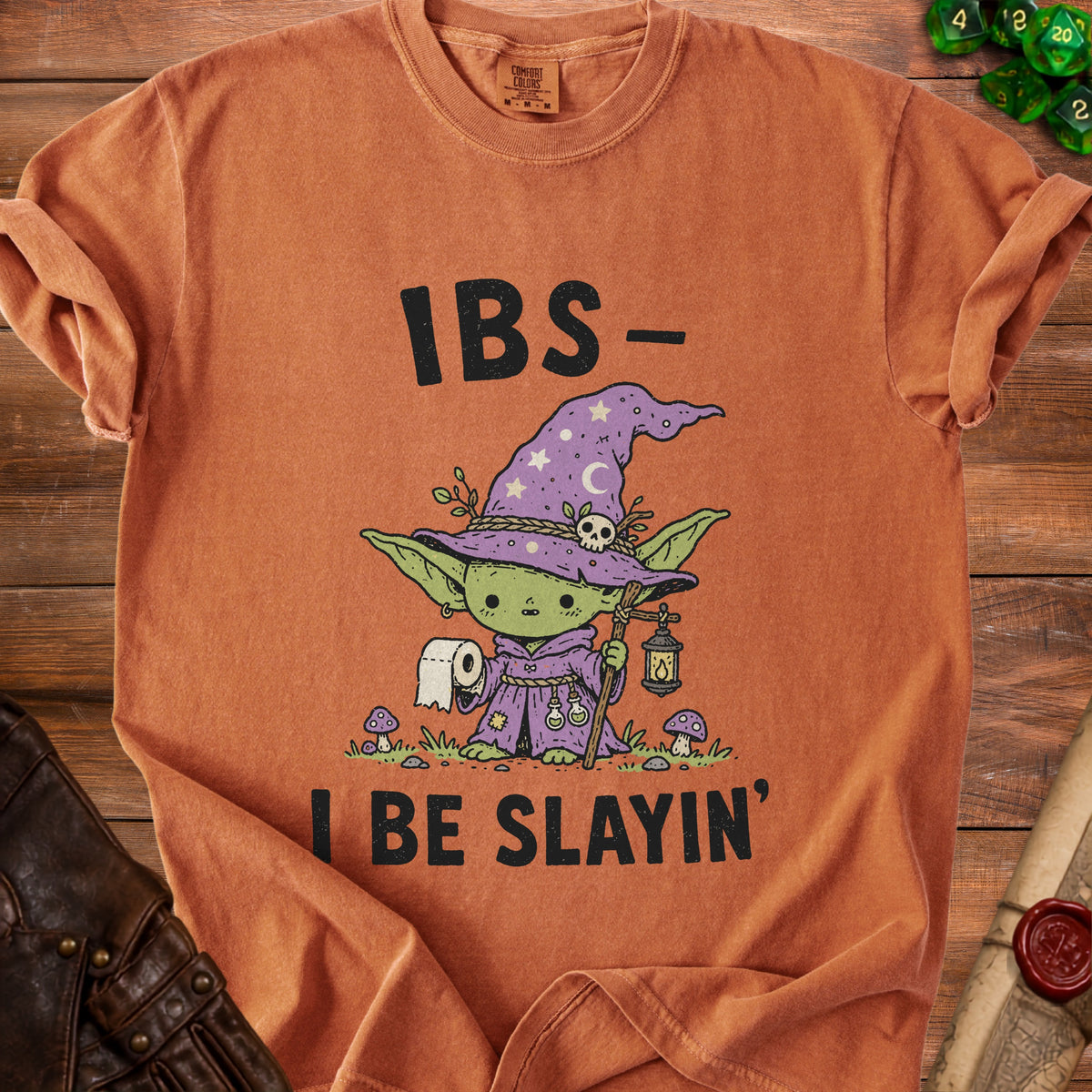 Orange t-shirt with a cartoon goblin in a witch hat holding toilet paper and a lantern.
