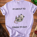 Purple t-shirt with a graphic of an opossum and text "IM ABOUT TO CRASH TF OUT."