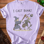 A wizard on a light purple t-shirt swings a club at a skeleton, with the text "I CAST BONK!".