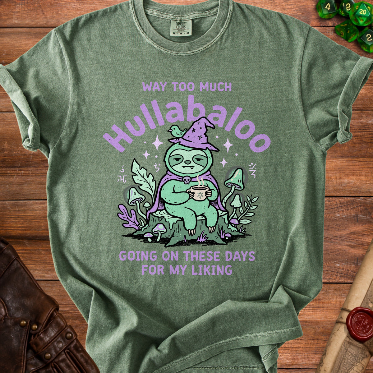 Green t-shirt with illustration of a sloth wearing a witch hat, holding coffee, and text "Hullabaloo".