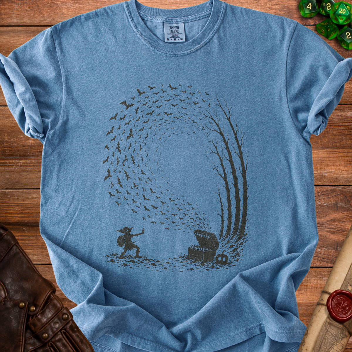 Blue t-shirt with dark graphic of a creature, treasure chest, bats, and trees.