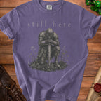 Purple t-shirt with knight and sword graphic and text "still here".