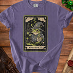 Purple t-shirt with a tarot card graphic of a frog wizard holding a lantern and a mug.