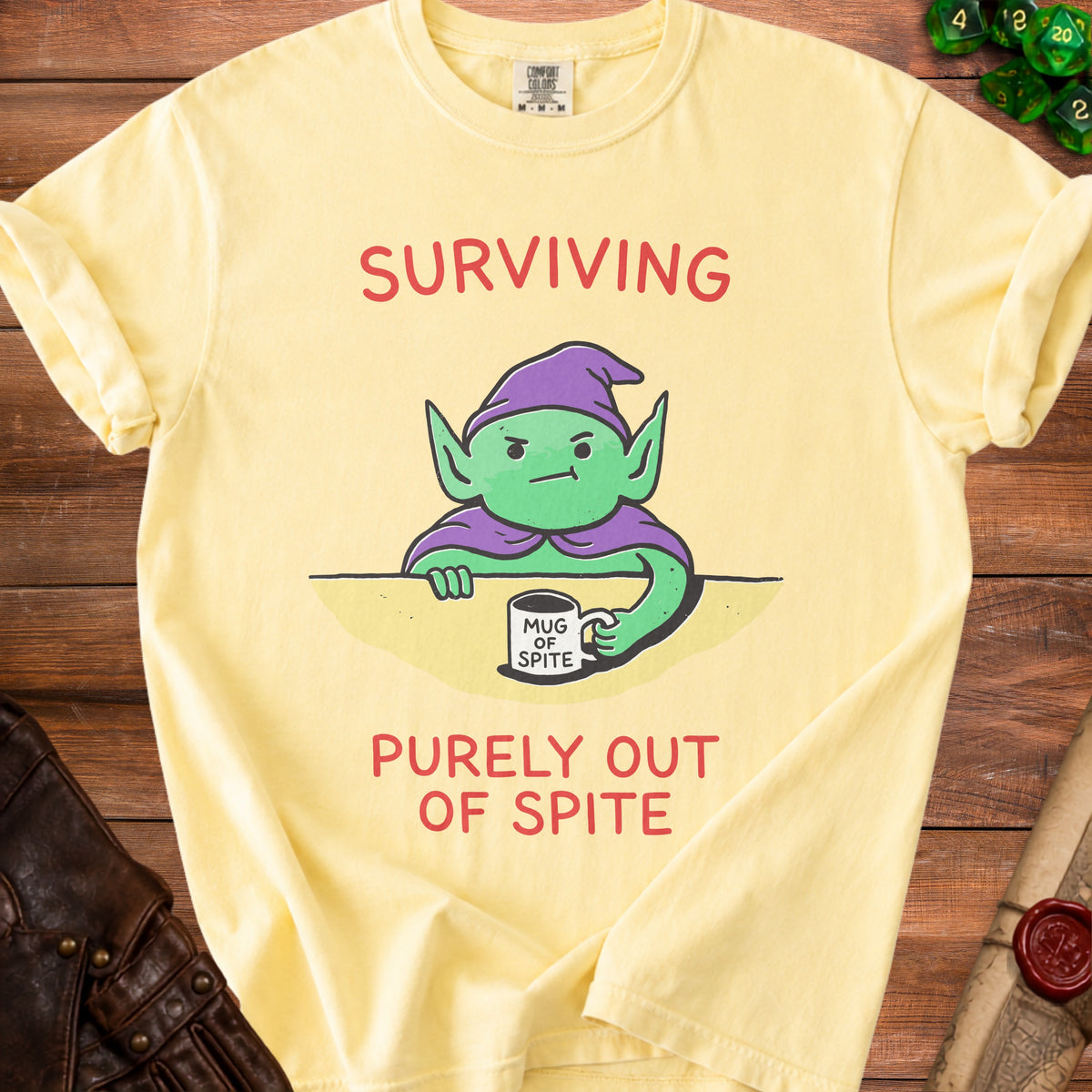 Yellow t-shirt with a cartoon goblin holding a mug that says "Mug of Spite" and text "Surviving Purely Out of Spite."