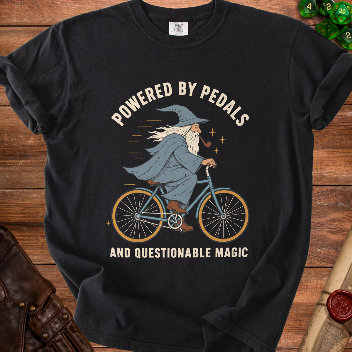 Black t-shirt with wizard on bicycle graphic and text "POWERED BY PEDALS AND QUESTIONABLE MAGIC".