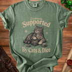 Green t-shirt with a cat and dice graphic reading "Emotionally Supported By Cats & Dice."