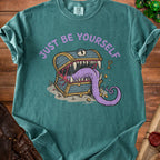 Teal t-shirt with purple text "JUST BE YOURSELF" and a monster treasure chest illustration.