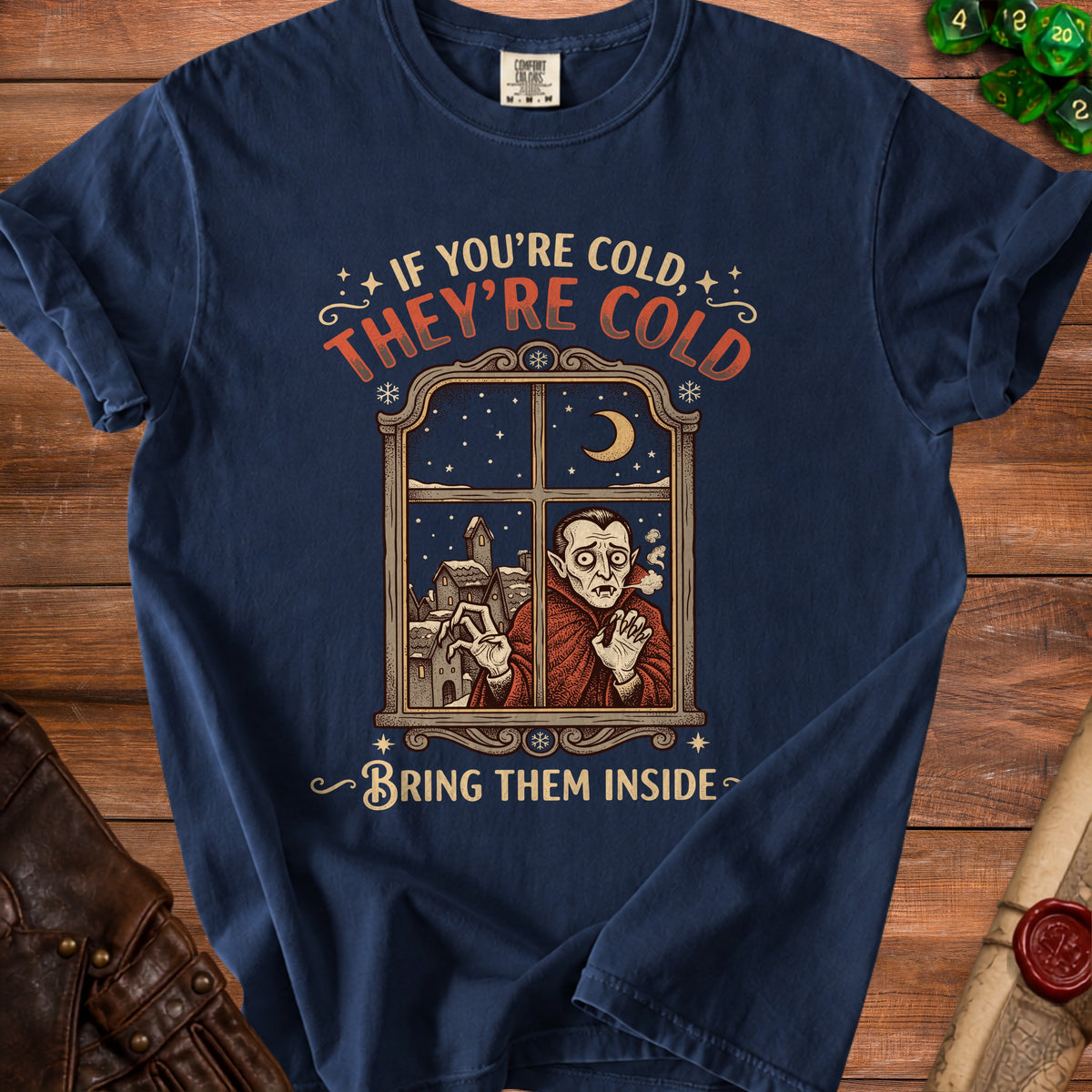 T-shirt with a vampire looking through a window at a snowy village. Text reads "If you're cold, they're cold, bring them inside."