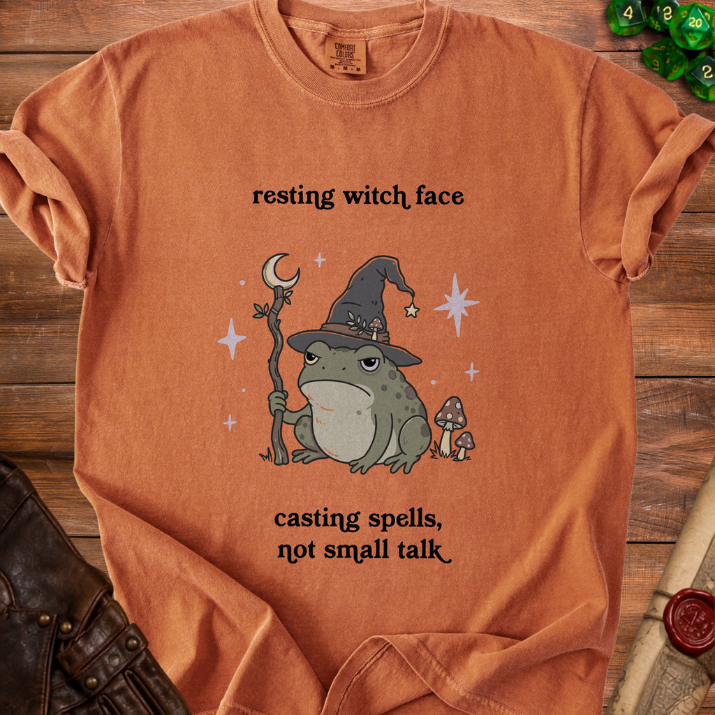 Orange t-shirt with a frog wearing a witch hat, holding a staff, and text "resting witch face, casting spells, not small talk".