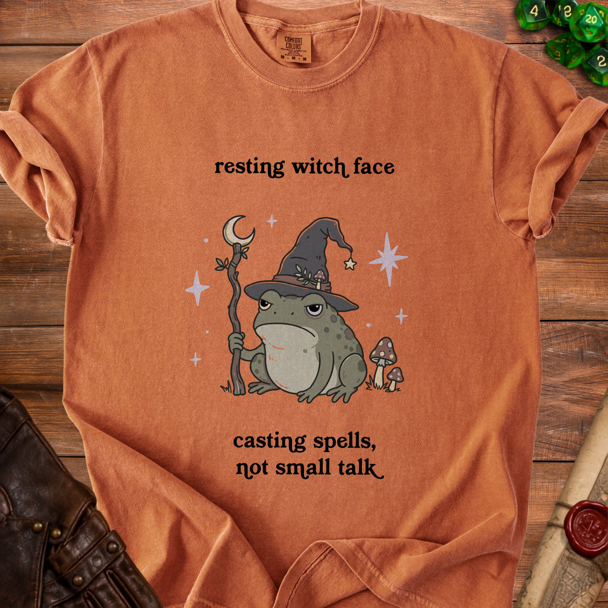 Orange t-shirt with a frog wearing a witch hat, holding a staff, and text "resting witch face, casting spells, not small talk".