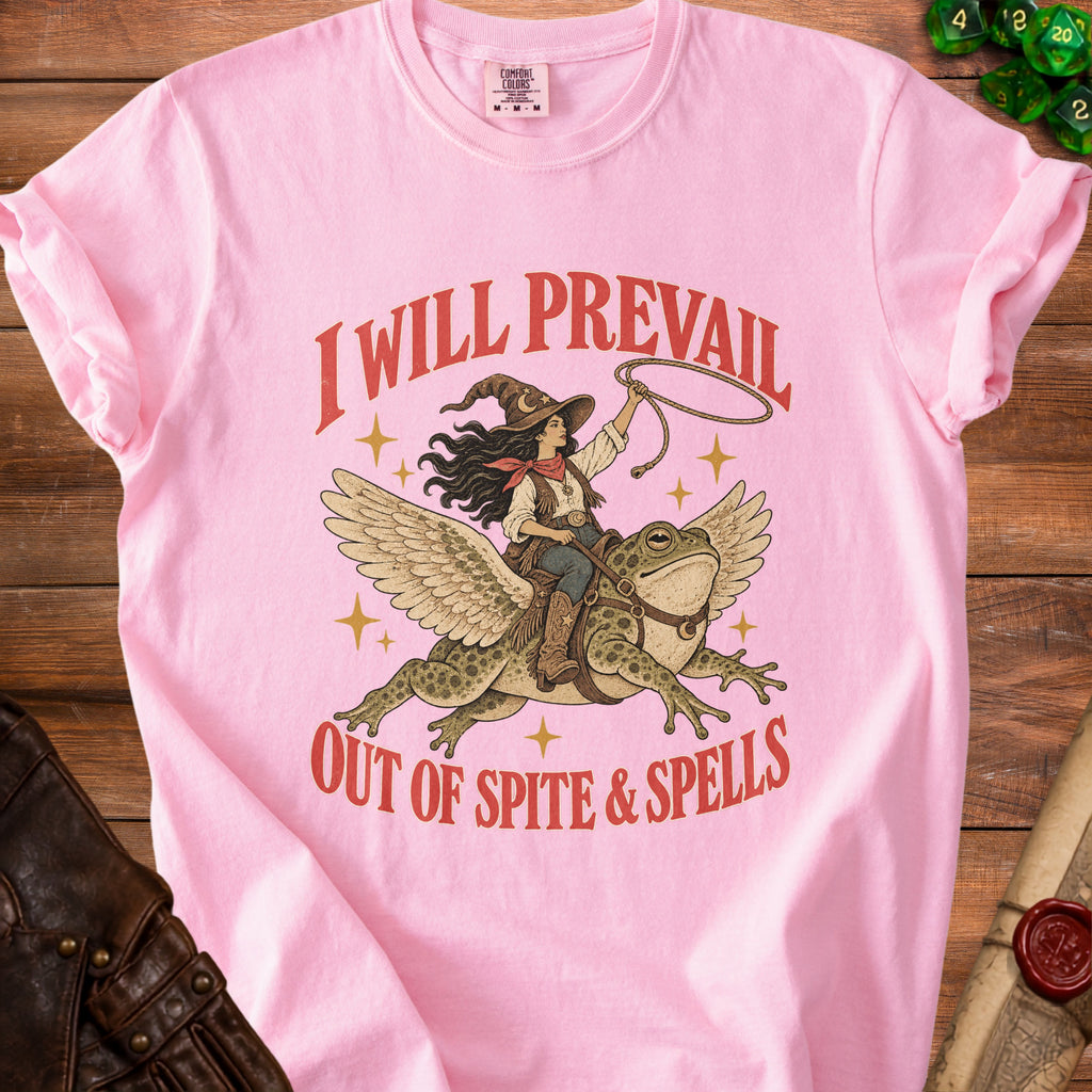 Pink t-shirt with a graphic of a cowgirl riding a winged frog, text "I WILL PREVAIL OUT OF SPITE & SPELLS".