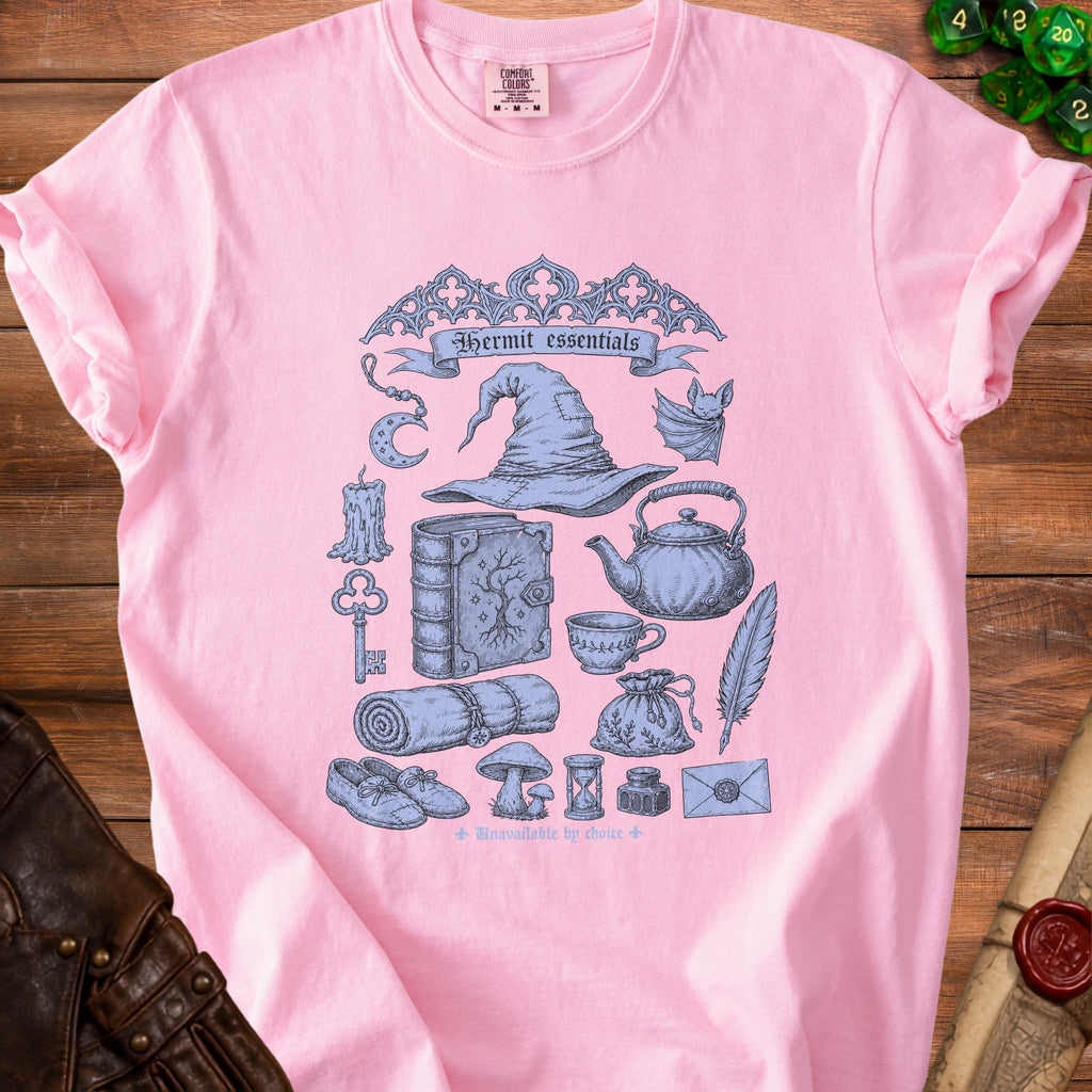 Pink t-shirt with a blue illustration of a wizard hat, bat, and other "Hermit essentials".
