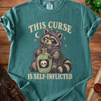 T-shirt graphic of raccoon drinking from bottle with skull, reads "THIS CURSE IS SELF-INFLICTED".