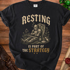 Black t-shirt with knight sleeping next to shield and sword, text "Resting is part of the strategy."