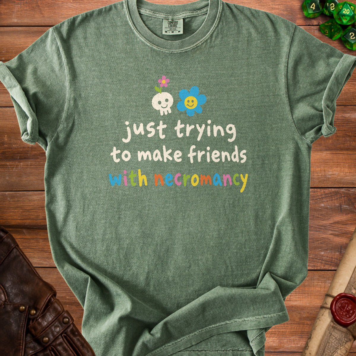 Green t-shirt with skull, flower, and text "just trying to make friends with necromancy".