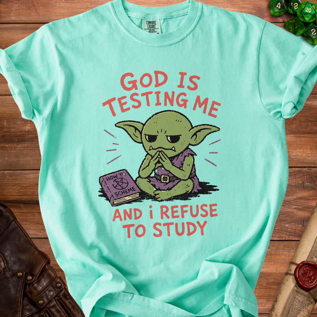 Green t-shirt with text "GOD IS TESTING ME AND I REFUSE TO STUDY" and a goblin illustration.