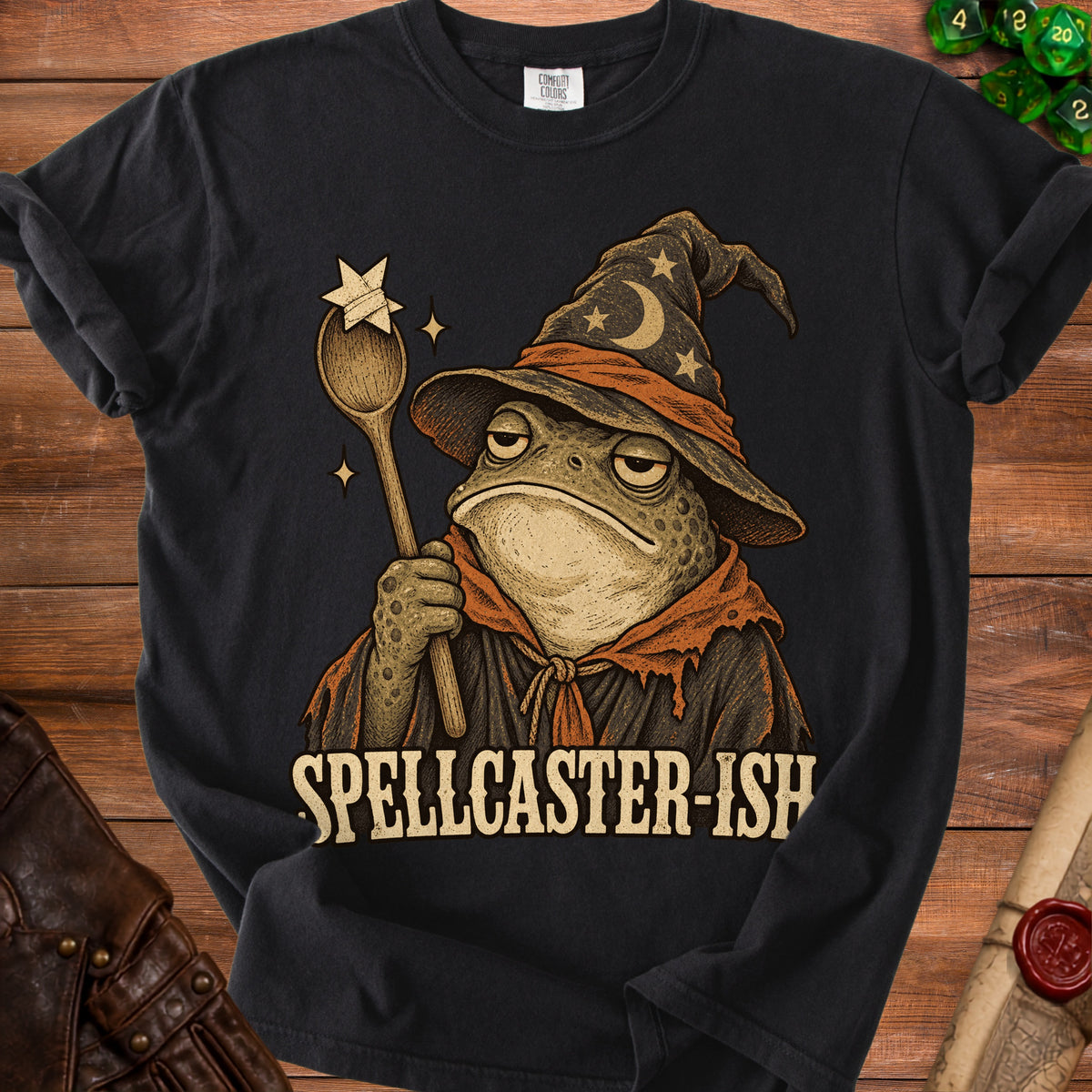 A black t-shirt features a graphic of a toad wearing a wizard hat and holding a wooden spoon, with the text SPELLCASTER-ISH below.