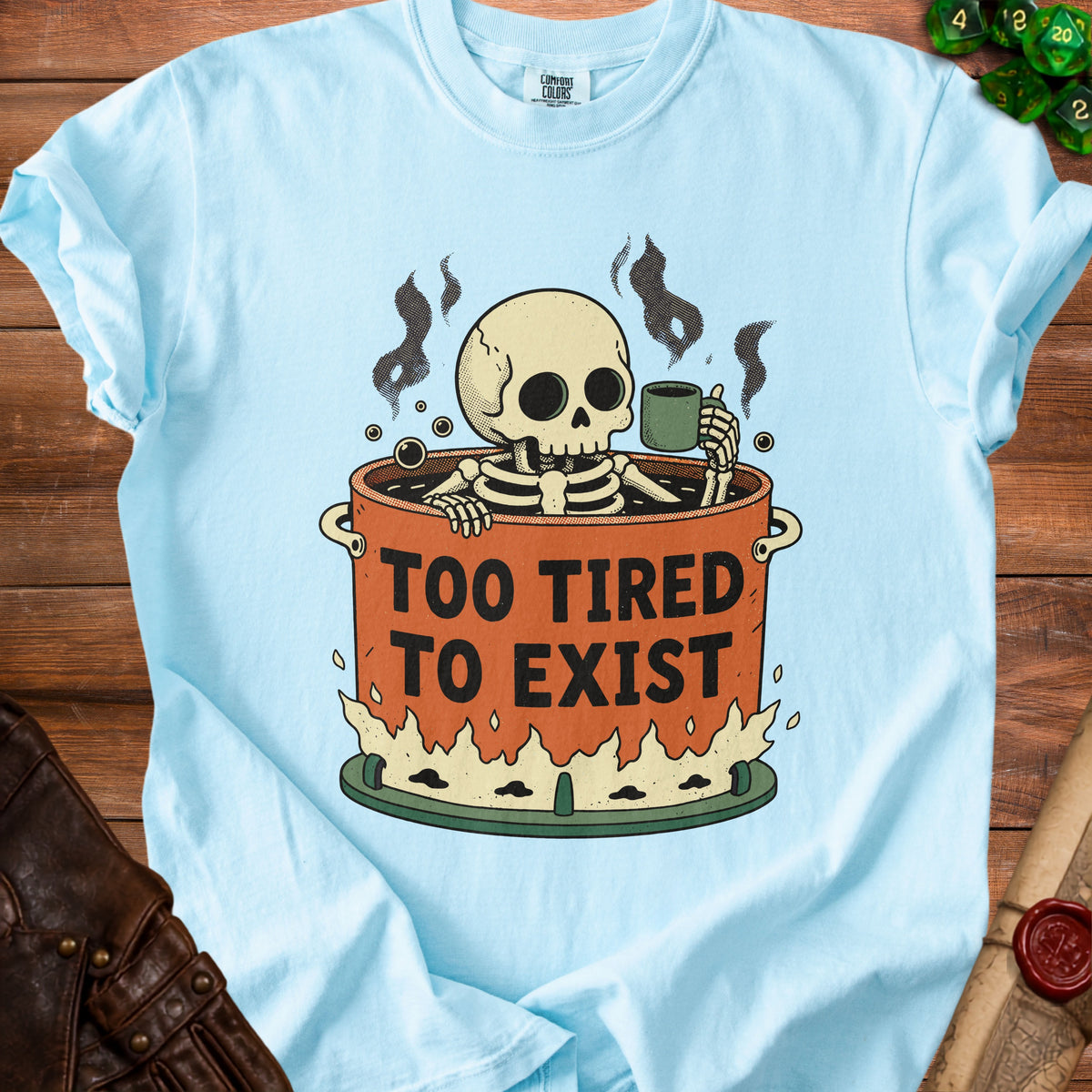 Light blue t-shirt with a skeleton in a pot of coffee, text "TOO TIRED TO EXIST".