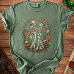 Muted green t-shirt featuring a vintage illustration of two skeletons dancing amidst a floral wreath.