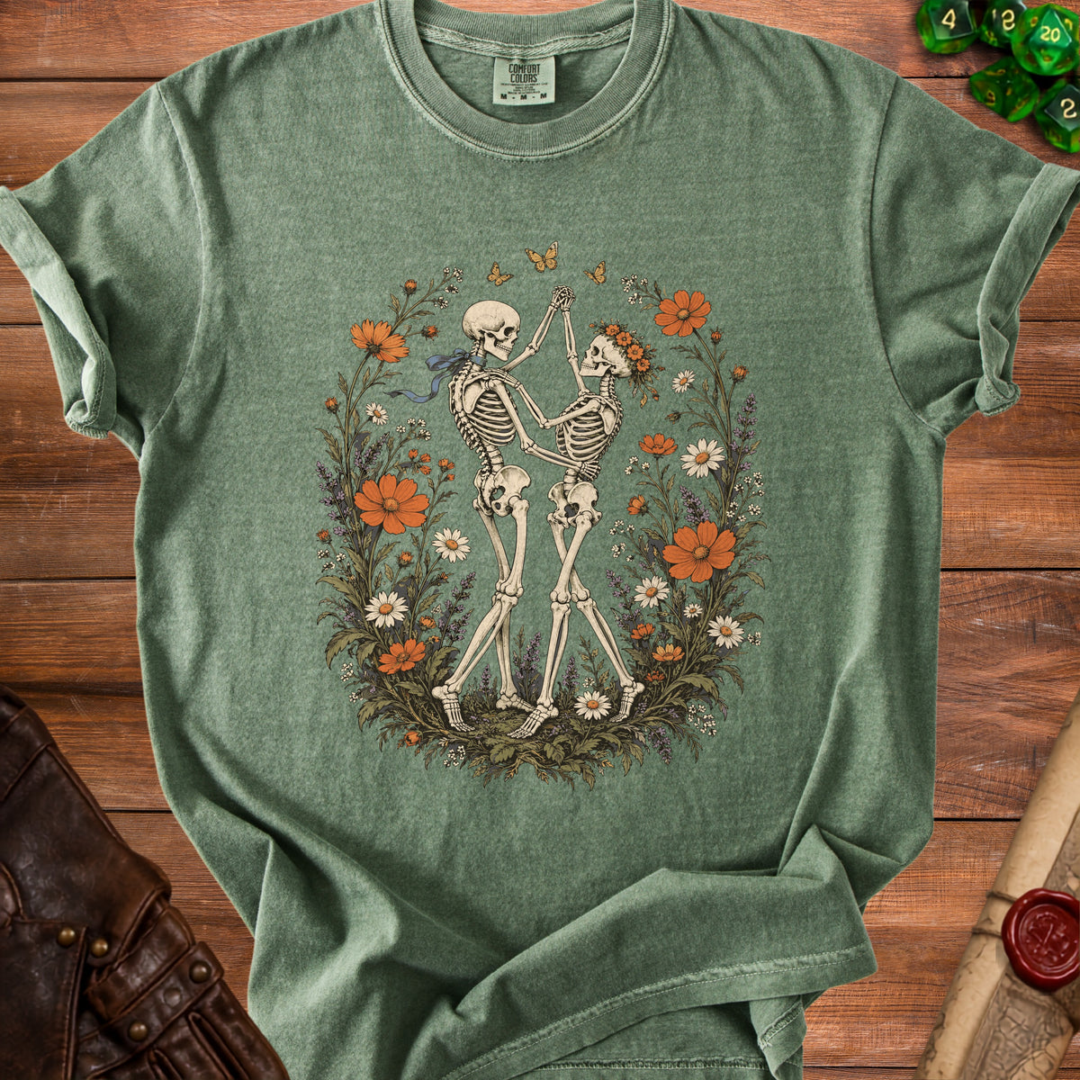 Muted green t-shirt featuring a vintage illustration of two skeletons dancing amidst a floral wreath.