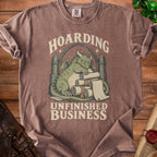 Brown t-shirt with a green dragon hoarding scrolls, reading "Hoarding Unfinished Business".