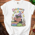 Black cat in witch hat reads "Existence Is Hard, But Books Help" on t-shirt.