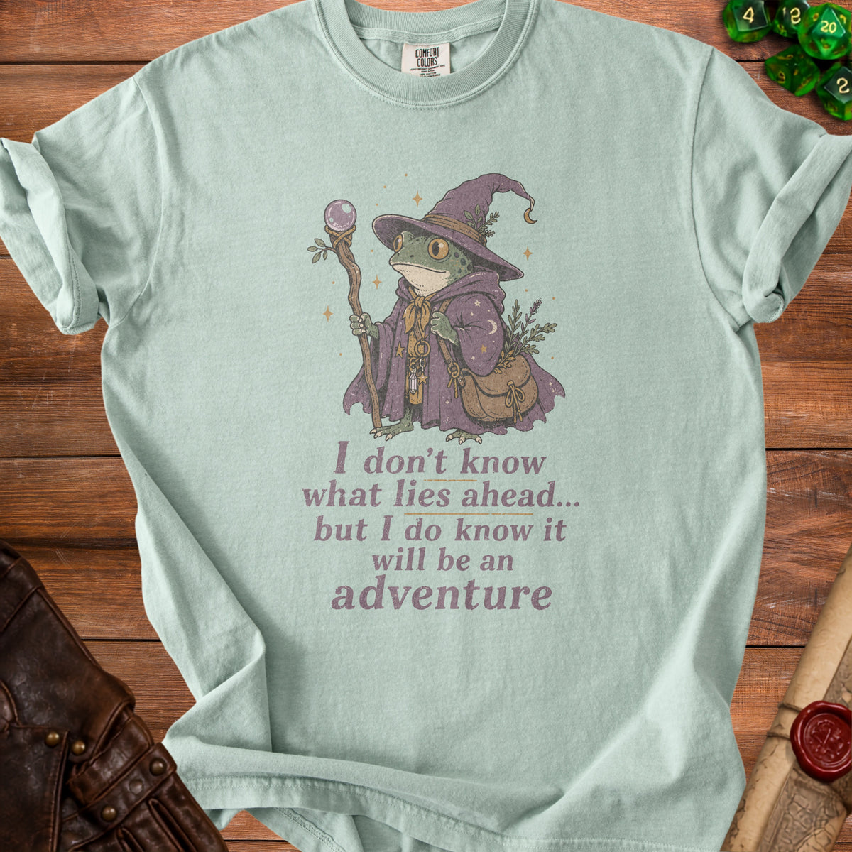 Light green t-shirt with wizard frog graphic and text "I don't know what lies ahead... but I do know it will be an adventure".