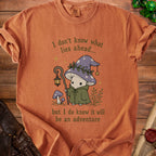 T-shirt with a mushroom character and the text "I don't know what lies ahead... but I do know it will be an adventure".