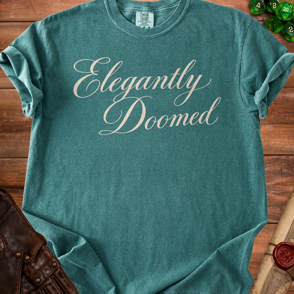 Teal t-shirt with "Elegantly Doomed" in cream script font.