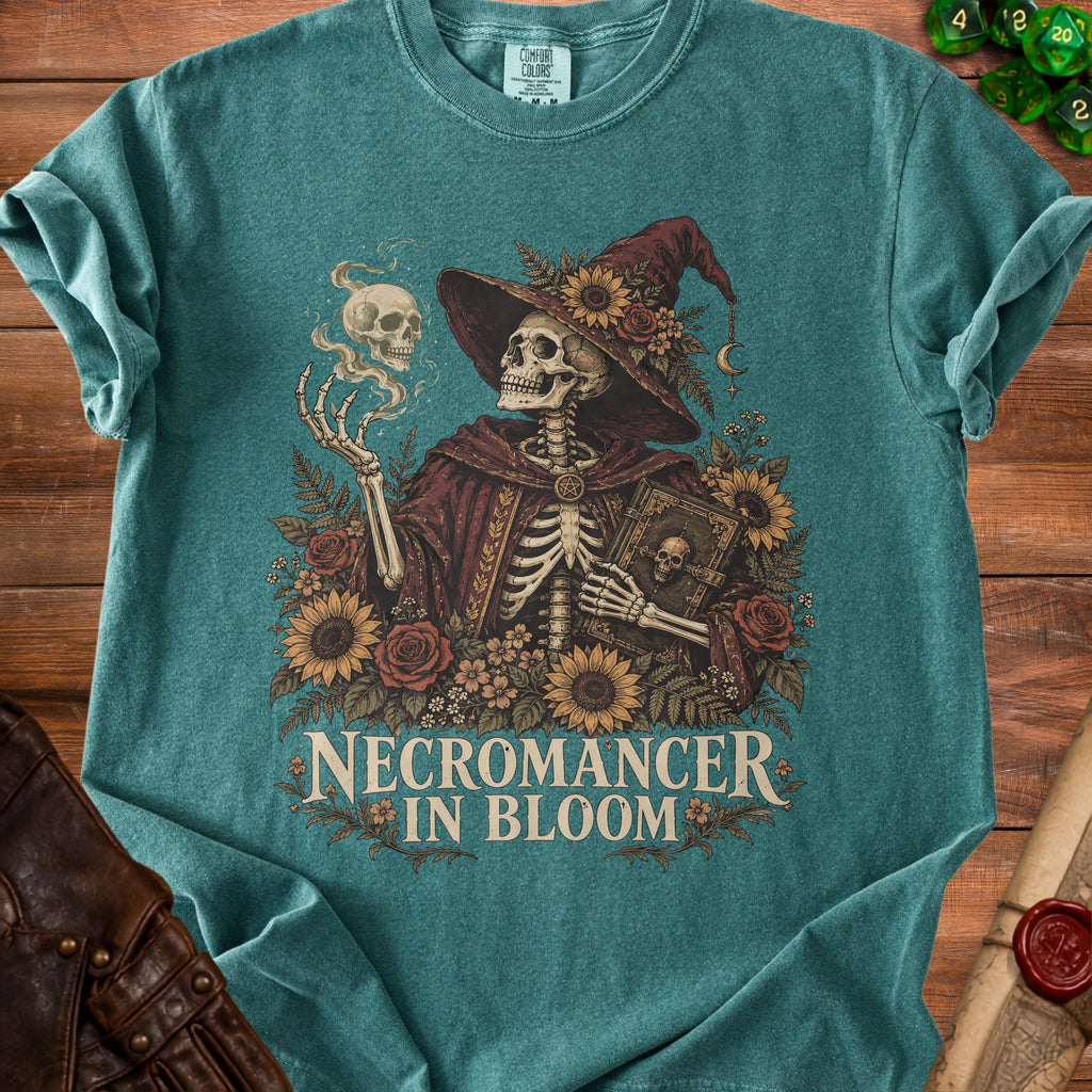 Teal t-shirt featuring a skeletal necromancer surrounded by flowers, holding a book, and text reading Necromancer in Bloom.